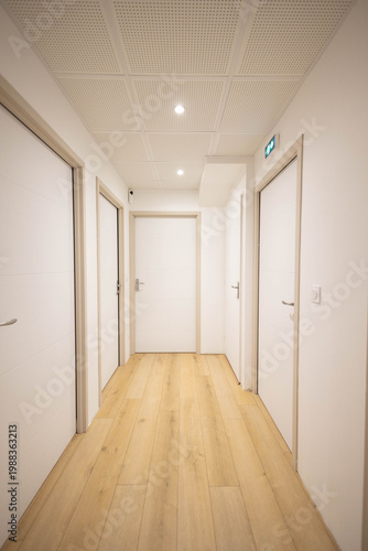 Un bureau, appartement neuf avec 5 portes fermées, les murs sont blancs et l'encadrement est en bois, le sol est un parquet en bois
