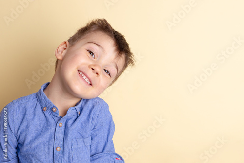 Boy of three years in a blue shirt on a yellow background. Emotional portrait.