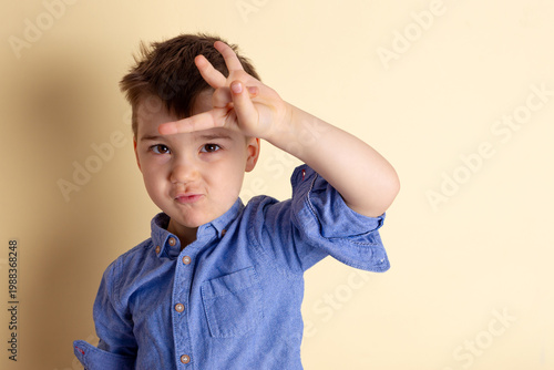 Boy of three years in a blue shirt on a yellow background. Emotional portrait.