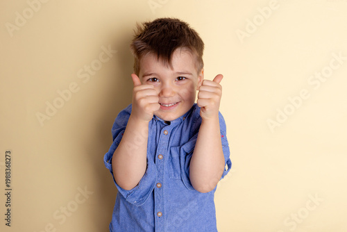 Boy of three years in a blue shirt on a yellow background. Emotional portrait.