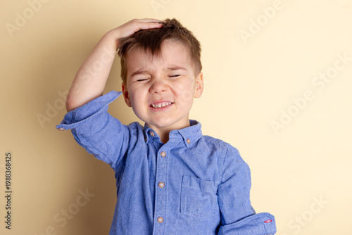 Boy of three years in a blue shirt on a yellow background. Emotional portrait.