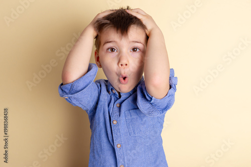 Boy of three years in a blue shirt on a yellow background. Emotional portrait.