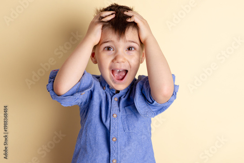 Boy of three years in a blue shirt on a yellow background. Emotional portrait.