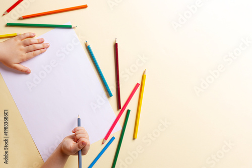 A boy draws with colored pencils on white paper.