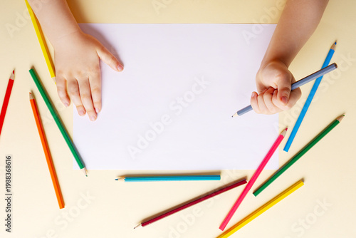 A boy draws with colored pencils on white paper.