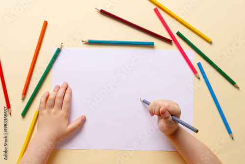 A boy draws with colored pencils on white paper.