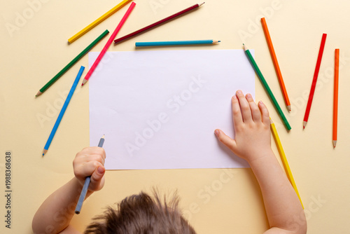 A boy draws with colored pencils on white paper.