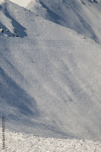 Snow-covered mountain slope shows ski tracks in winter at a ski resort during daylight hours