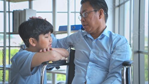 A little son speaks encouragingly to his father, who is seated in a wheelchair