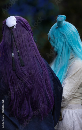 Back view of two cosplayers with long purple and turquoise hair at an anime convention