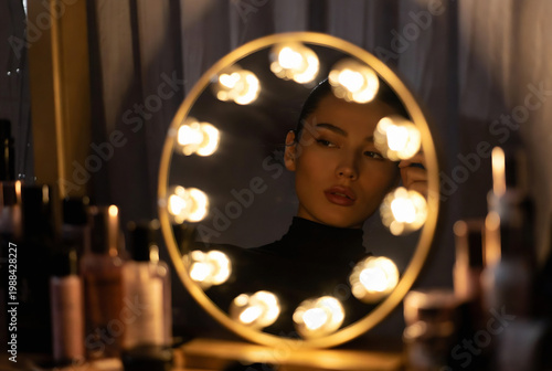 A woman is reflected in a circular vanity mirror with lights, likely applying makeup. The setting appears to be a luxurious hotel room or spa area.