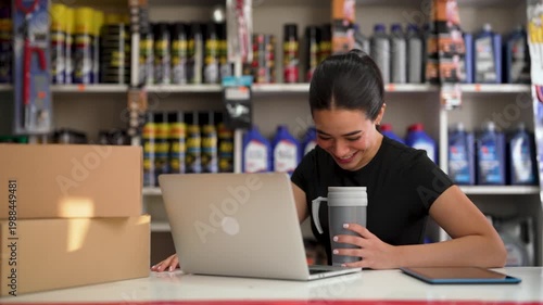 Young female business owner working on a laptop and laughing during a video call in her store