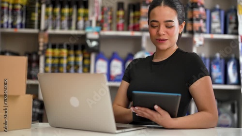 Smiling woman entrepreneur using a tablet and laptop to manage her small business inventory