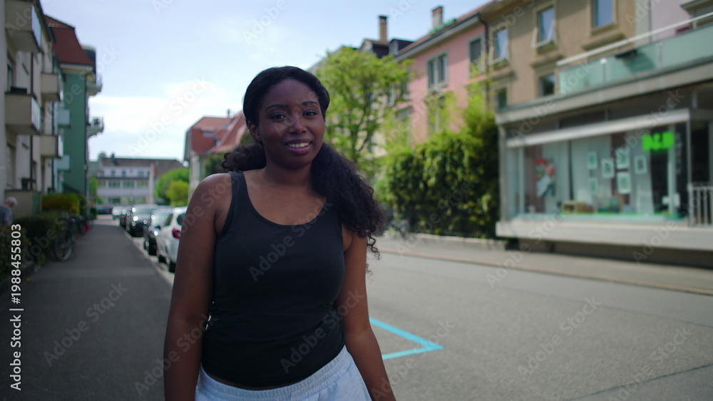 Fototapeta premium African American woman standing on residential street smiling toward camera creating warm and approachable urban lifestyle moment in everyday outdoor environment