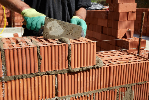 Tableau sur toile A skilled bricklayer is carefully applying mortar to red bricks, aligning them p