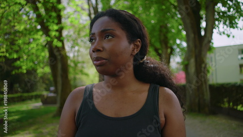 African American woman standing in park holding her head and showing visible stress, worry and preoccupation creating tense and emotionally charged outdoor lifestyle moment in natural environment