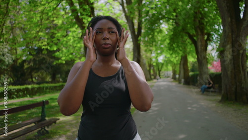 Foto African American woman standing in park holding her head and showing visible str