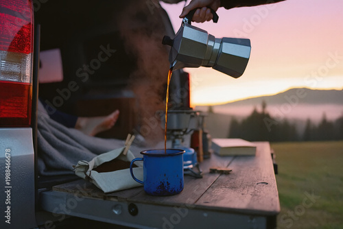 Steam rises as fresh coffee is poured from a moka pot into an enamel mug on a van tailgate. Misty mountain sunrise background. Cozy scene of a morning brew and the quiet freedom of a trip in the wild