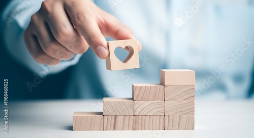 Wooden blocks staircase with heart icon, hand placing heart block on top of wood stack, concept of building love and relationship growth