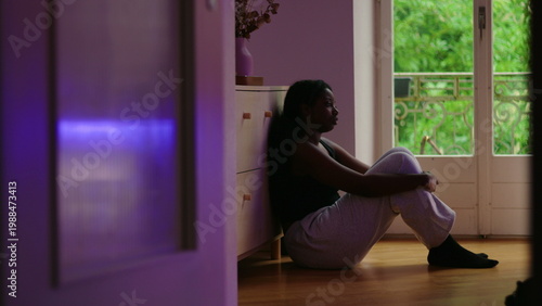 Fotografie African American woman wide shot sitting on floor by window leaning against cabi