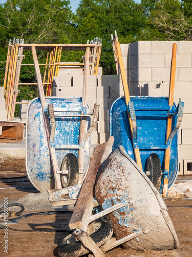 Three well-used masonry wheelbarrows, one on its side and two upright, for concrete work on a house construction site in a suburban residential development in southwest Florida. Workplace at a glance.