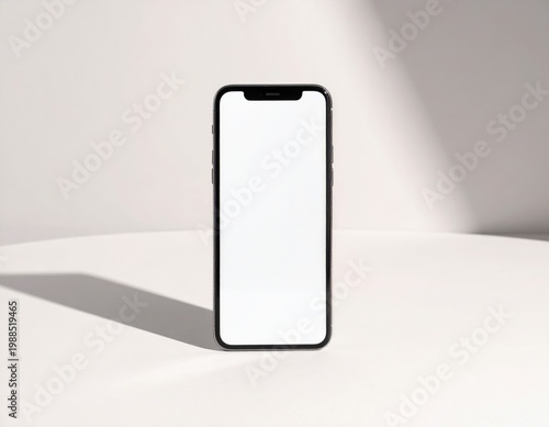 Modern black smartphone with a blank white screen stands upright on a clean white surface showcasing soft, natural shadows, perfect for a content display or app presentation
