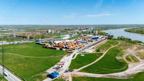Aerial view of the vibrant container depot with the Sava River gently curving by, contrasted against the lush greenery, Sremska Mitrovica, Vojvodina, Serbia.