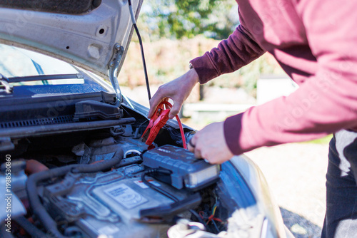 Fotografía Young man using jumper cables to boost a car battery under the hood on a sunny d
