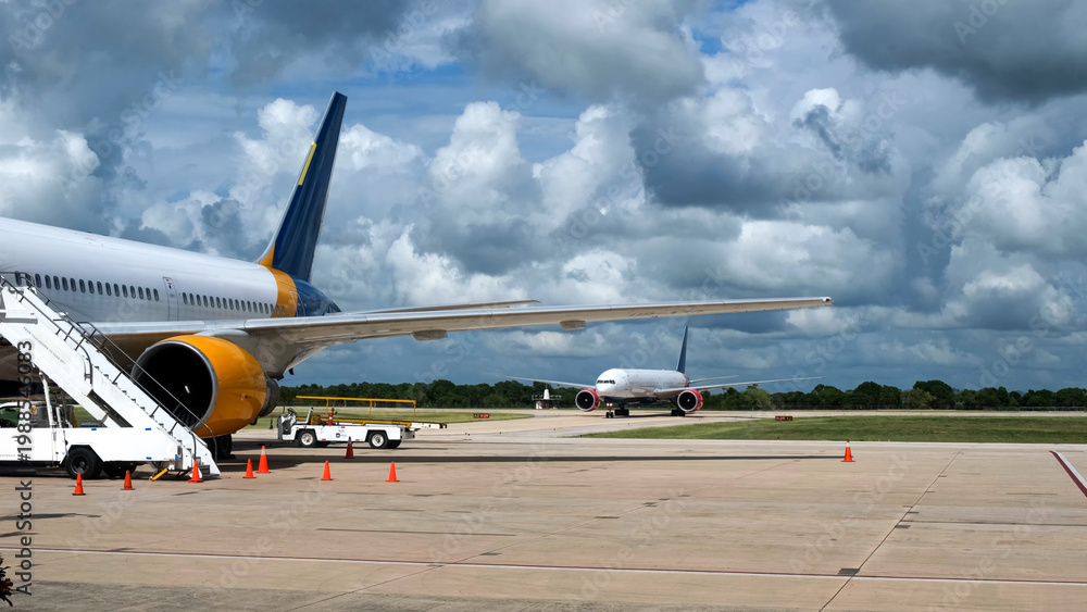 Obraz premium Airplanes parked on tarmac at an airport with a staircase leading to the cabin and clouds in the blue sky, showcasing aviation infrastructure and operations