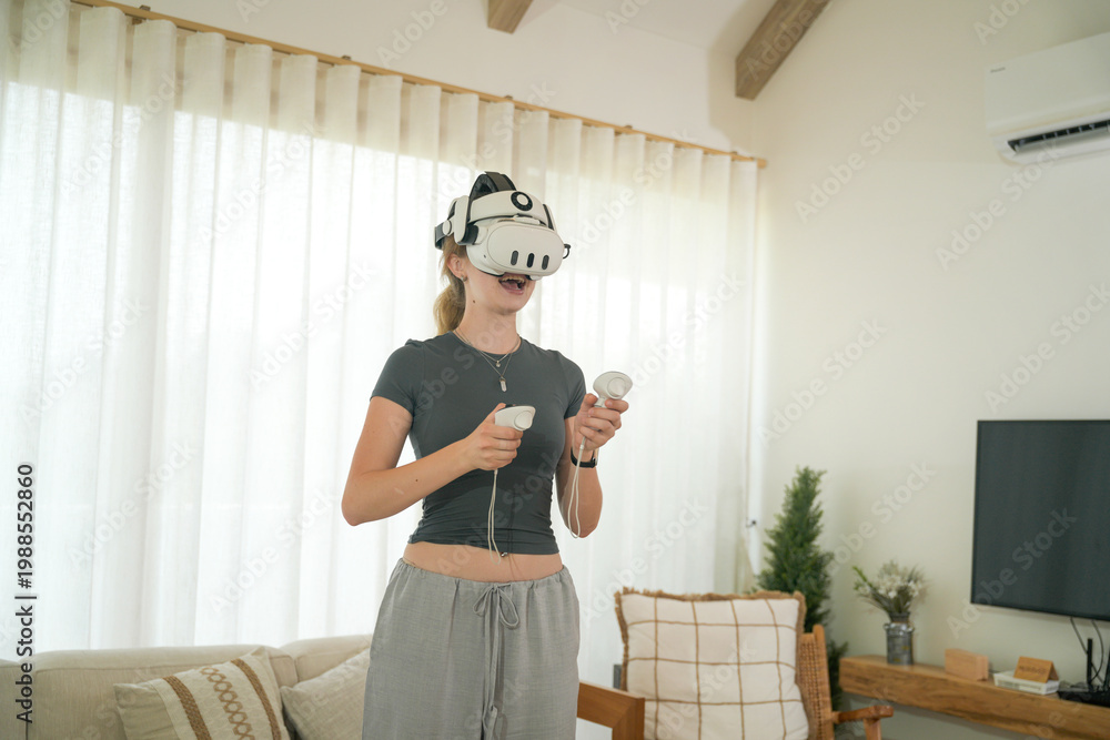 Fototapeta premium Young woman wearing a VR headset and playing a video game with controllers