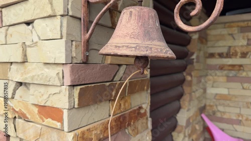 Decorative antique bell fixed on coarse stone wall with frayed rope