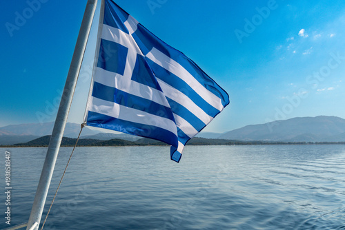 Greek Flag Flying Over Calm Sea and Distant Mountains