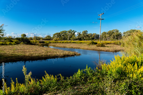 Small creek through meadow with power pole under blue sky