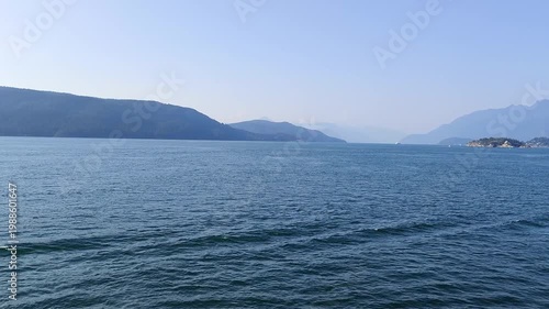 At Sea - View across tranquil waters towards coastal mountains. A peaceful seascape featuring the calm sea and mountainous land in the background.