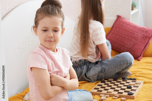 Foto Two sisters playing checkers on a bad and having small fight