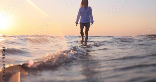 Happy woman is walking on the sandy beach in a red dress against sunrise. Slow motion