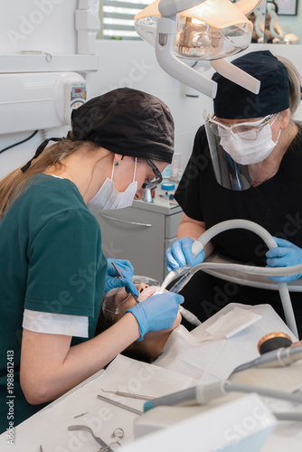 Professional medical team of dentist and assistant treating patient in stomatology clinic. Specialists using drill and suction for tooth care, oral surgery and hygiene procedure.