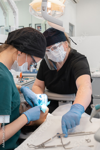 Dentist and assistant working together for professional dental treatment and tooth surgery. Stomatology team treating patient in clinic using isolation system and surgical lamp equipment.