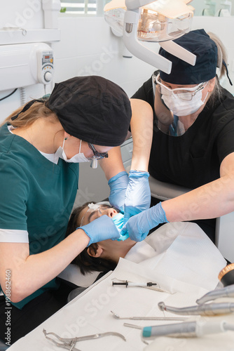Professional dentist using dental floss for blue latex rubber dam isolation on patient tooth. Female assistant helping during medical procedure in stomatology office. Oral hygiene care.