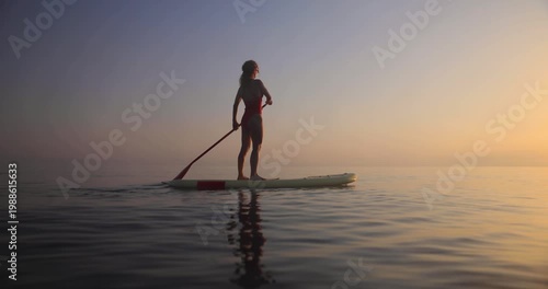 A happy young woman walking on a sup board by the sea during her summer vacation. Slow motion
