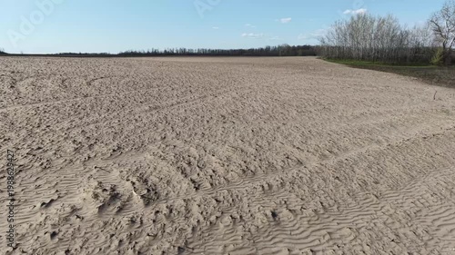 Drone shot showing soil erosion patterns on agricultural field. Contrast between fertile dark earth and light eroded sandy patches on cultivated land under clear sky in countryside.