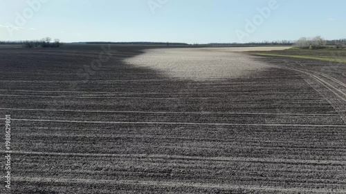 Drone shot showing soil erosion patterns on agricultural field. Contrast between fertile dark earth and light eroded sandy patches on cultivated land under clear sky in countryside.