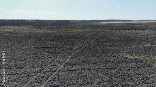 Drone shot over vast agricultural land showing wind erosion and dust patterns on dry soil. Wide panoramic view of cultivated black earth with light sandy sections. Process of soil degradation.
