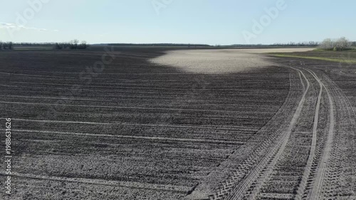 Drone shot showing circular tire patterns on plowed farmland. High contrast between dark soil and large light eroded patches under clear sky. Soil degradation problem.