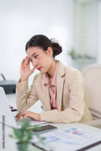 stressed Asian businesswoman feeling headache tension while working with laptop computer reading financial report document at modern office workspace suffering from work pressure