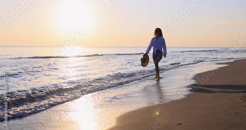 Happy woman is walking on the sandy beach in a red dress against sunrise. Slow motion