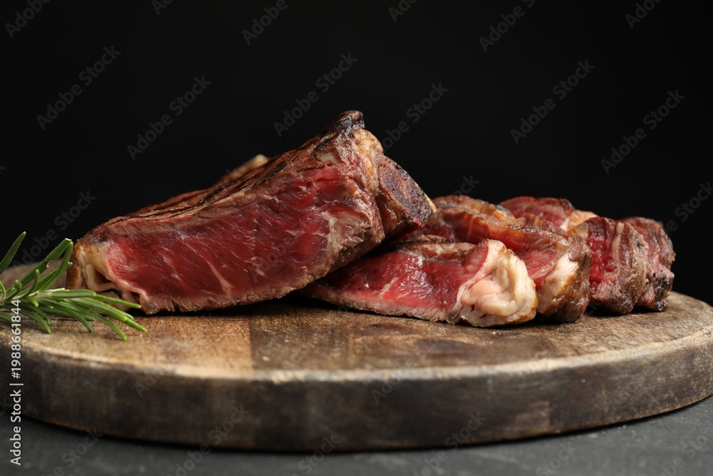 Fototapeta premium Pieces of tasty beef steak with rosemary on table against black background, closeup