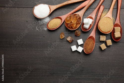 Fotografie Different types of sugar in spoons on wooden table, flat lay