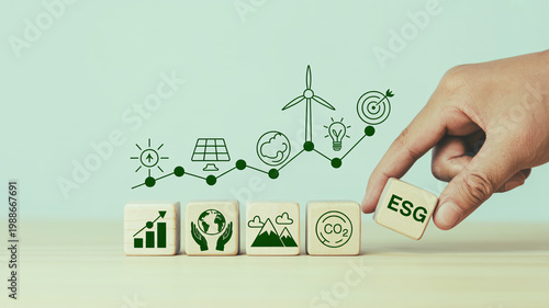 A hand placing an ESG block among environmental icons and graphs on wooden cubes