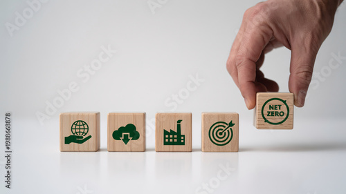 A hand placing a wooden block with a net zero symbol on a table with other eco-friendly blocks
